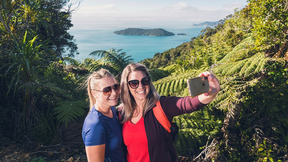 Two women take a selfie at a viewpoint on the northern Queen Charlotte Track in the Marlborough Sounds, New Zealand.