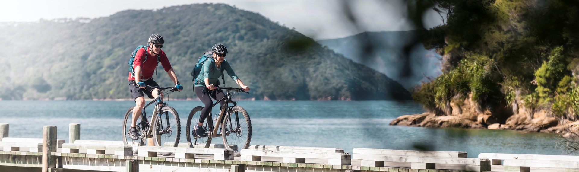 A male and female biking along the Ship Cove/Meretoto jetty at the start of the Queen Charlotte Track