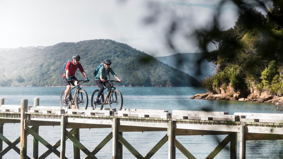 A male and female biking along the Ship Cove/Meretoto jetty at the start of the Queen Charlotte Track