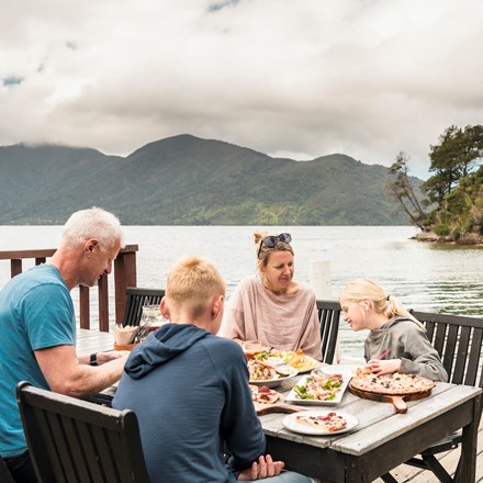 A family dining on the jetty at Punga Cove - a great way to enjoy stone baked pizza and more at the Boatshed Cafe and Bar.