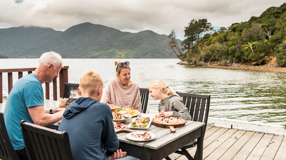 A family dining on the jetty at Punga Cove - a great way to enjoy stone baked pizza and more at the Boatshed Cafe and Bar.