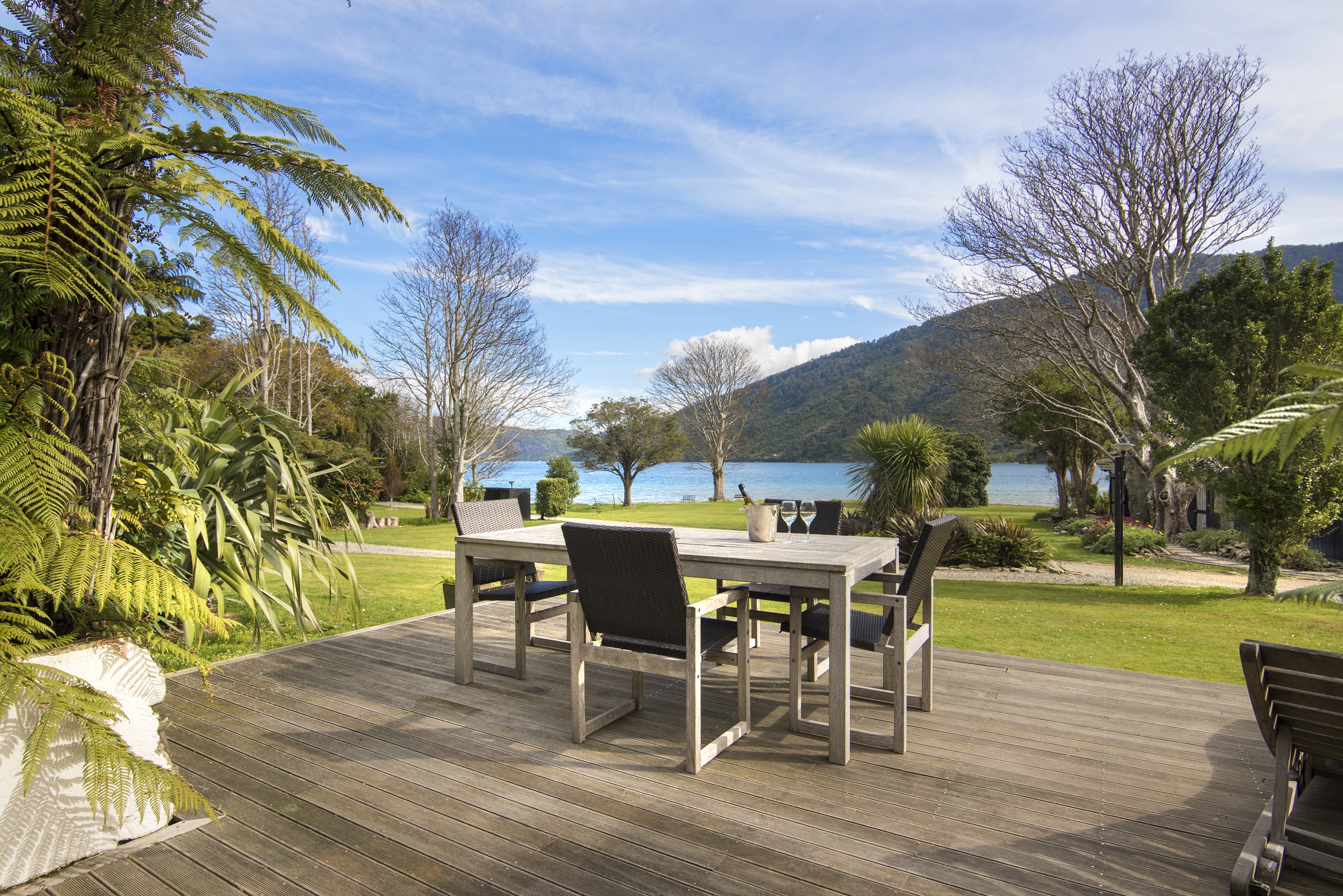 The view from a Cook's Cottage at Furneaux Lodge overlooks the furnished outdoor deck, sweeping green lawn and Endeavour Inlet in the Marlborough Sounds, New Zealand