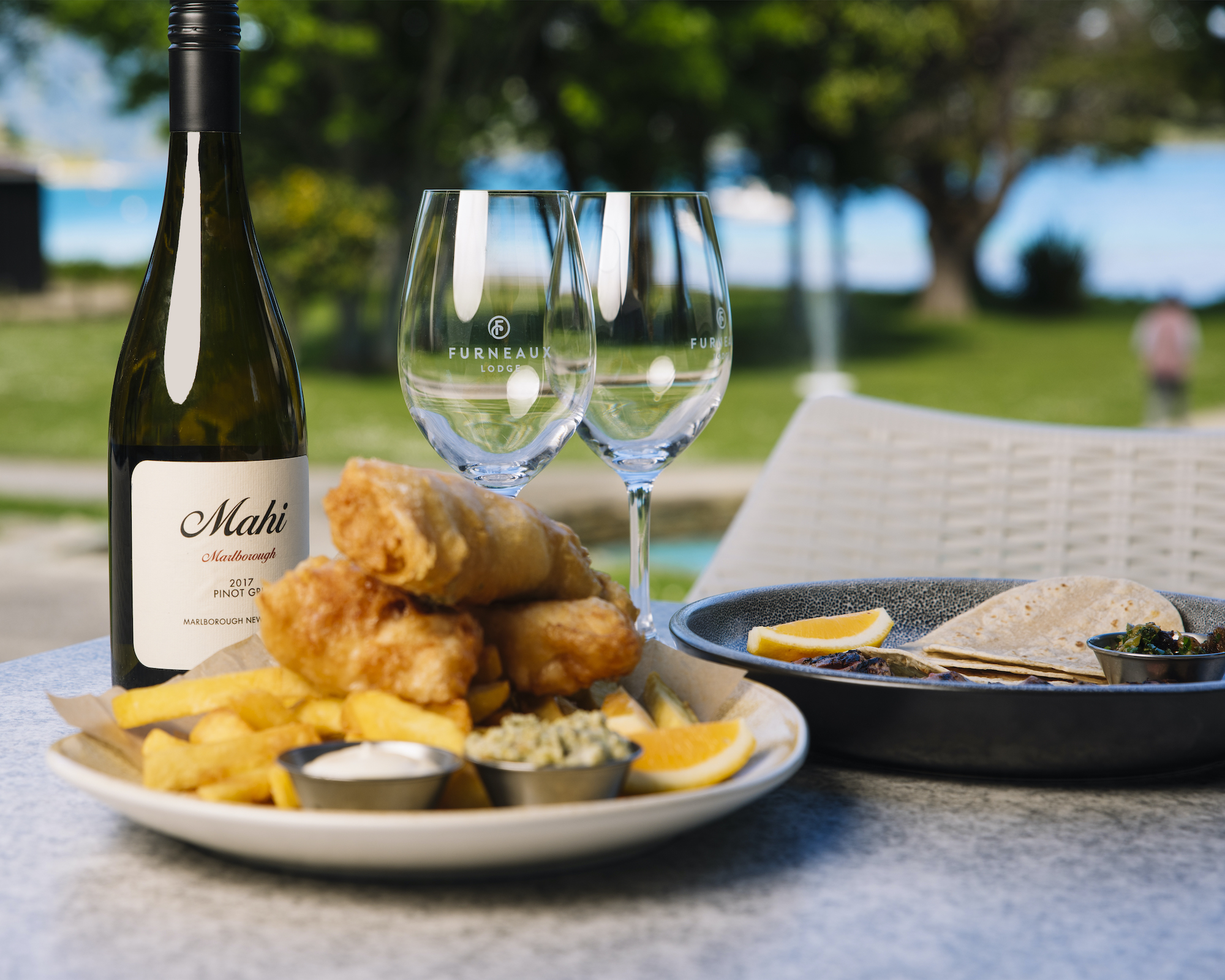 Furneaux Lodge's famous fish and chips with bottle of wine glasses and view of the water.