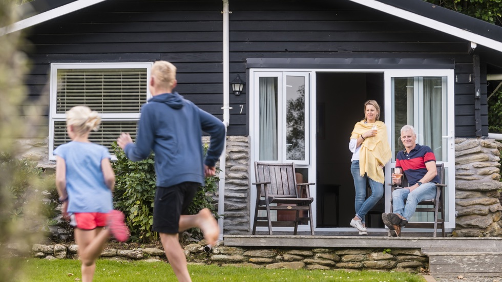 Two children run on the lawn of Furneaux Lodge while their parents watch from a Cook's Cottage with a glass of wine in the Marlborough Sounds, New Zealand.