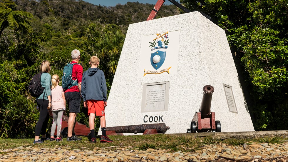 Four people look at the monument to Captain James Cook at Ship Cove/Meretoto in the Marlborough Sounds, New Zealand.