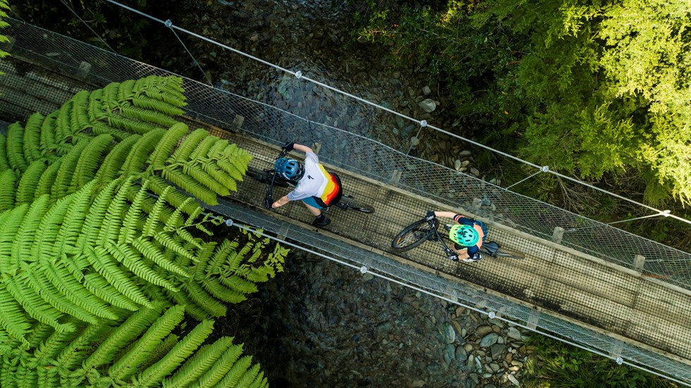 Two mountain bikers cross a swing bridge on the northern Queen Charlotte Track in the Marlborough Sounds, New Zealand.